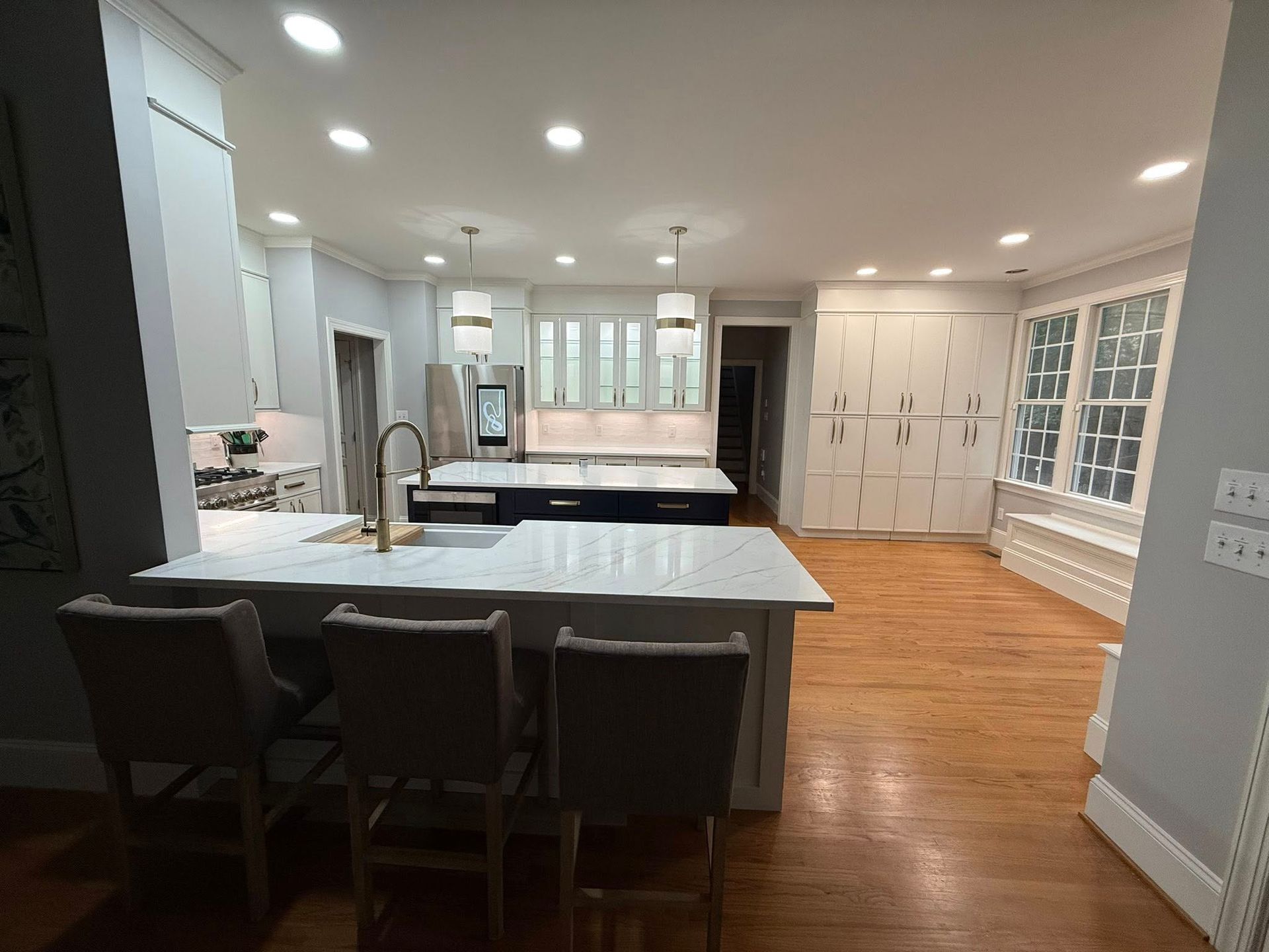 Spacious kitchen with island seating, white countertops, dark blue island, stainless steel appliances, and wooden floors.