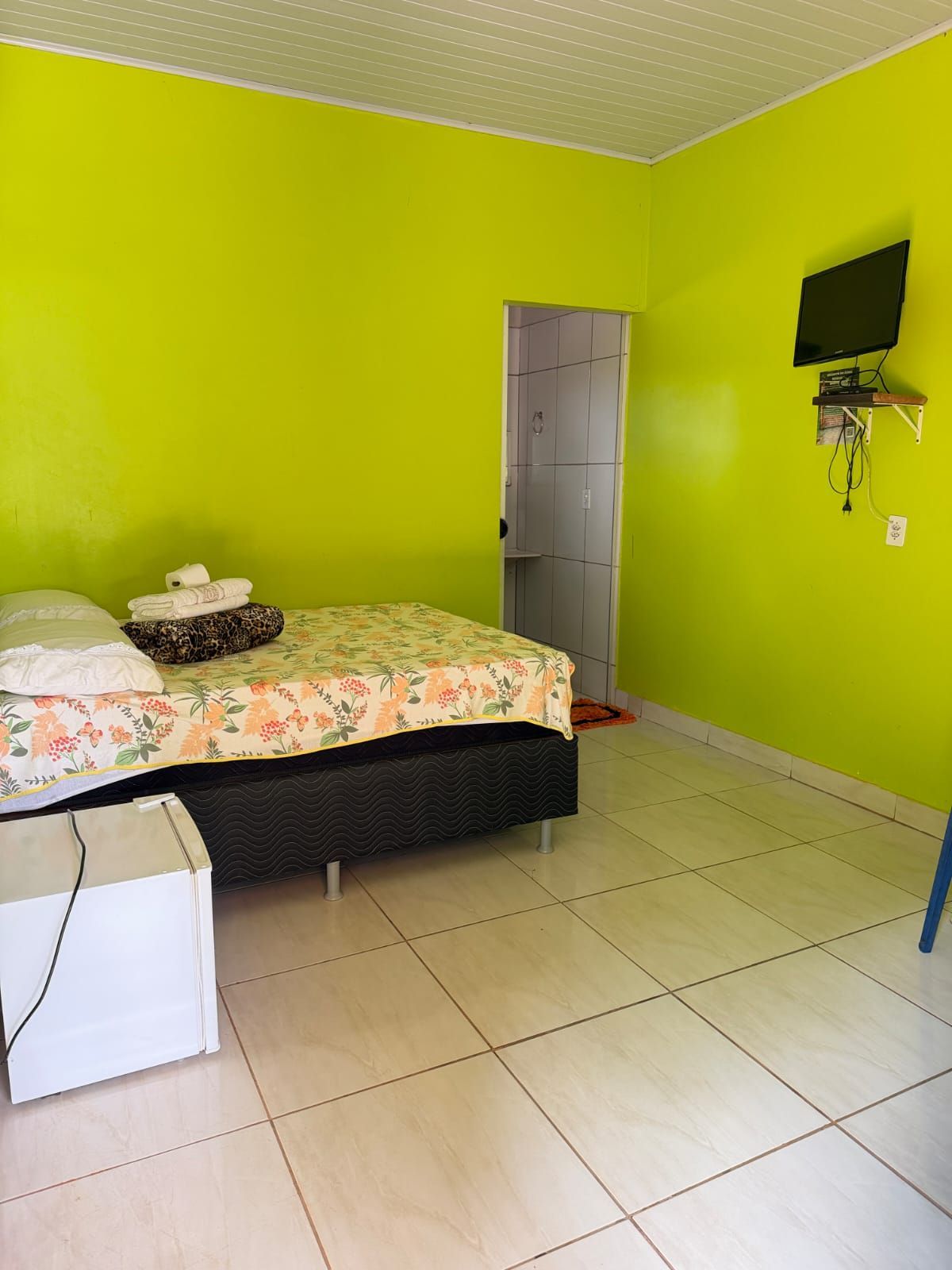 Um pequeno quarto com paredes verde-lima vibrantes, piso de azulejo, uma cama com roupa de cama floral