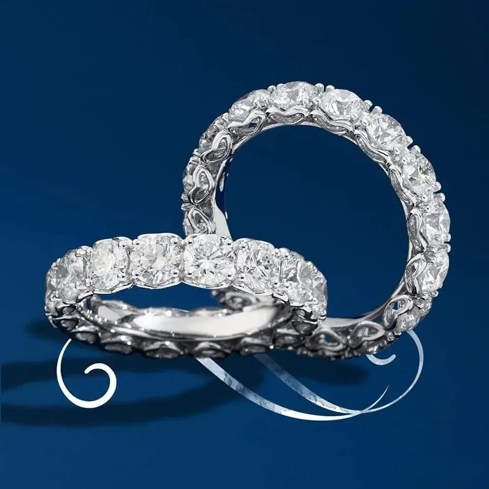 Due anelli dell'eternità con diamanti su sfondo blu, che riflettono la luce.