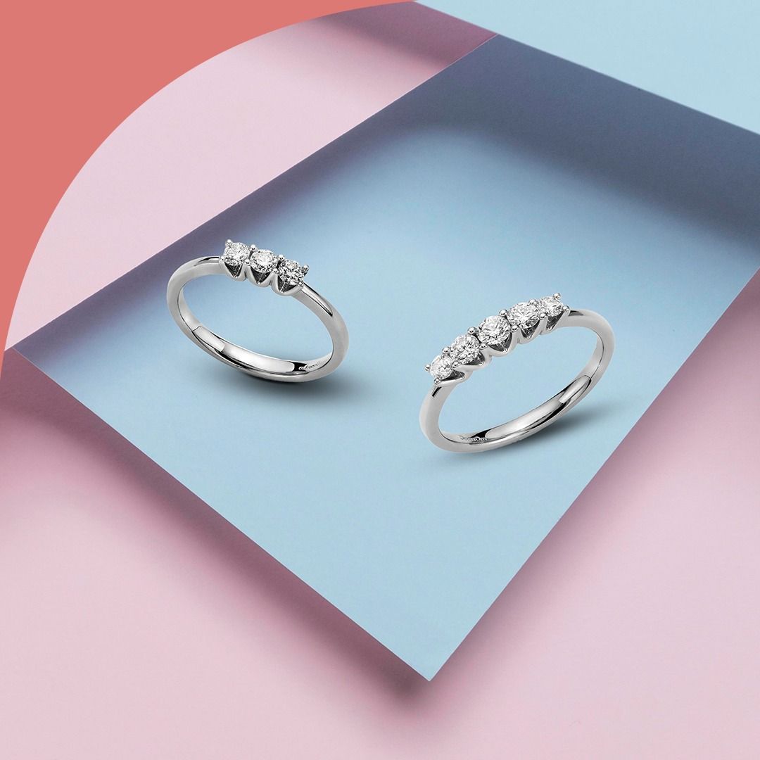 Due anelli in argento con diamanti su sfondo blu e rosa.