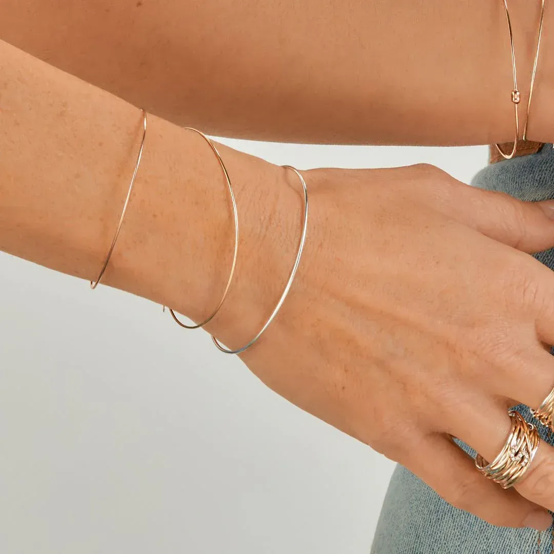 Polso e mano di donna con tre sottili braccialetti d'argento, dita con anelli sovrapposti, indossa jeans blu.