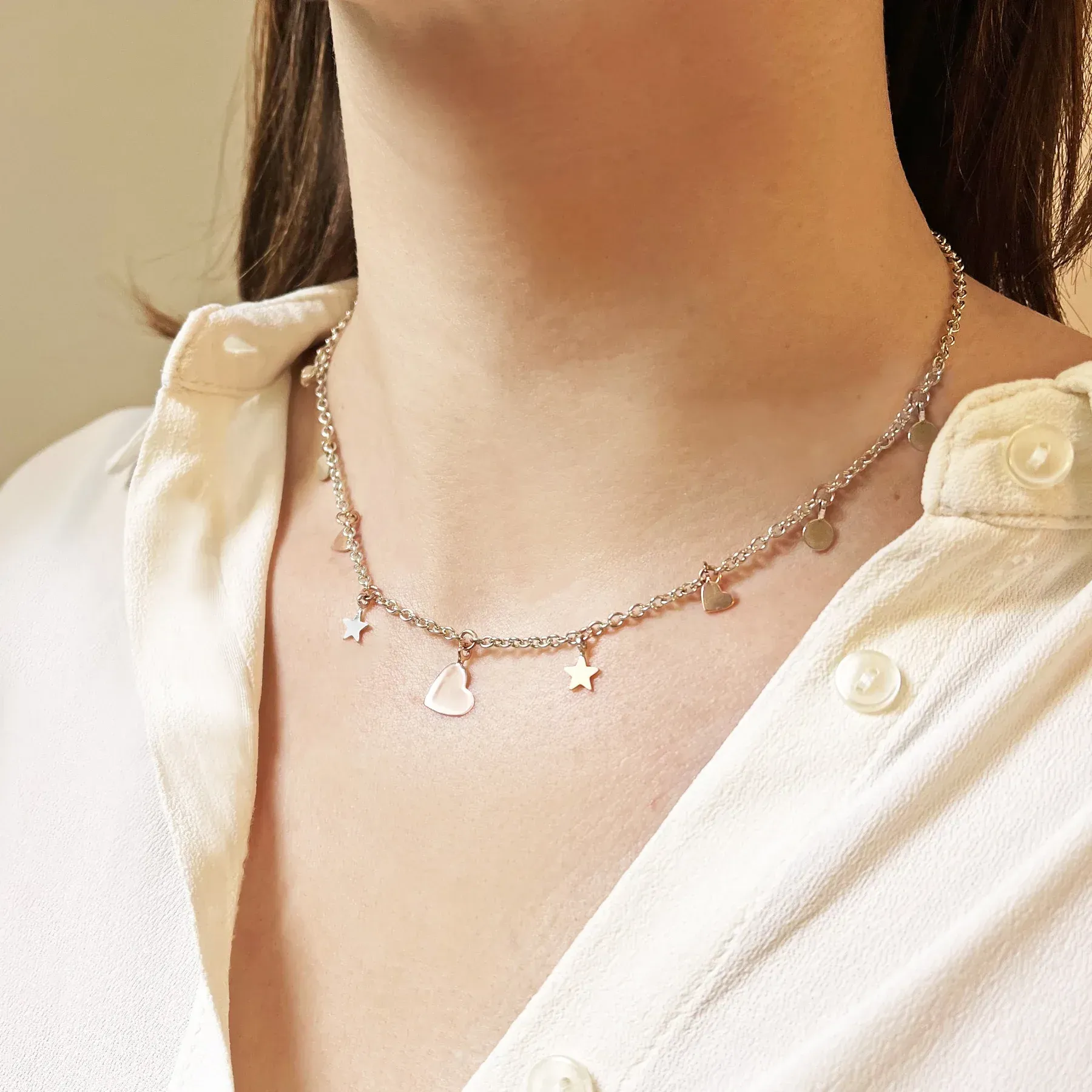 Donna che indossa una collana in argento con ciondoli a forma di stella, cuore e uccello, sopra una camicetta bianca.