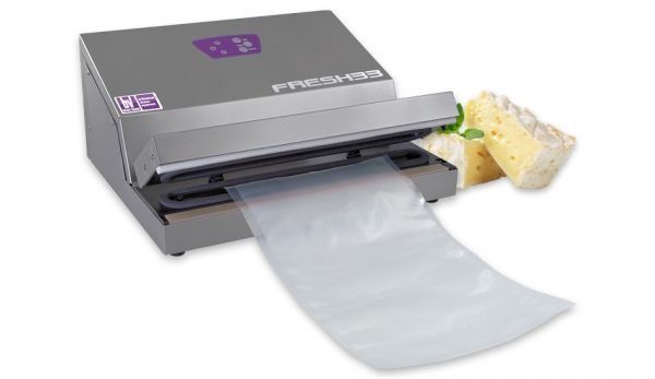 Una macchina sottovuoto grigia per alimenti sigilla un sacchetto di plastica contenente cibo, con un rotolo di pellicola trasparente che fuoriesce.