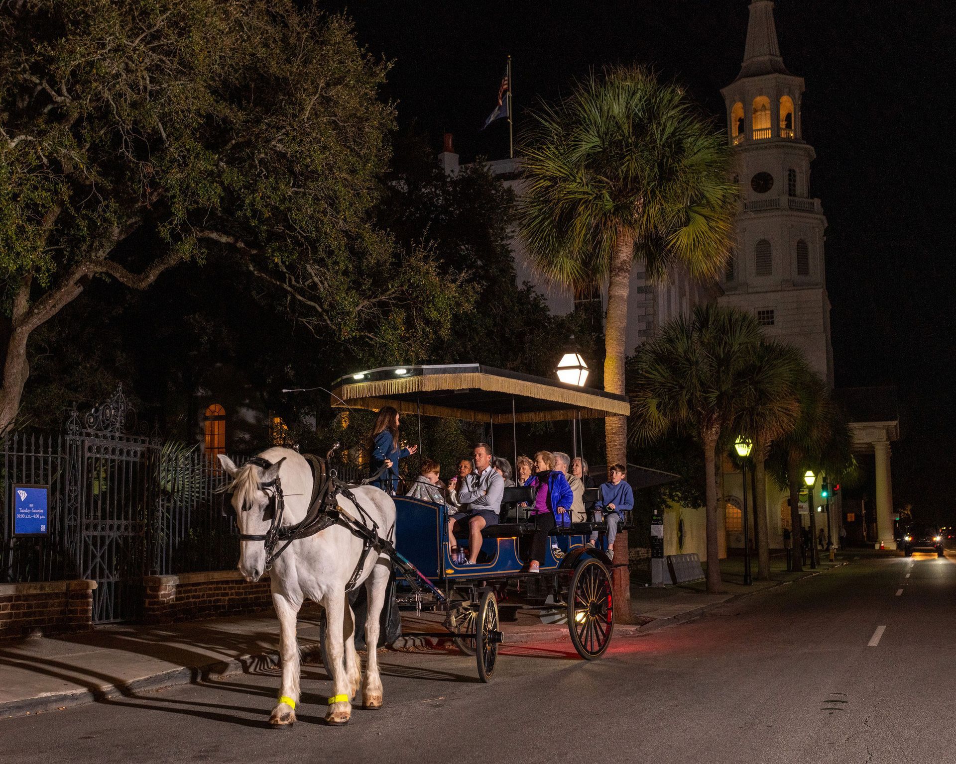 A horse drawn carriage with people in it is driving down a street at night.