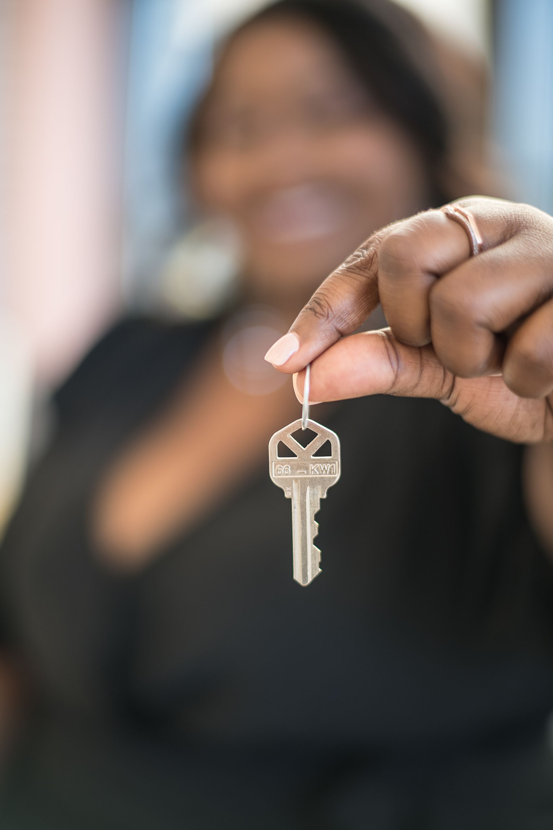 Hand holding a key in front of a blurred person in a dark top