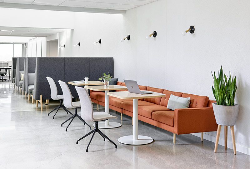 Modern office lounge area with orange sofa, small tables, and white chairs.