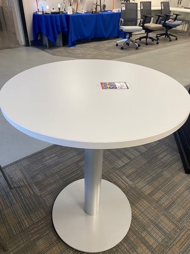 White round table with a silver pedestal base on a patterned rug.
