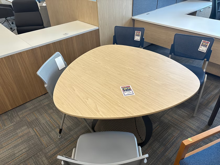 A triangular light wood table with four chairs, in an office setting.