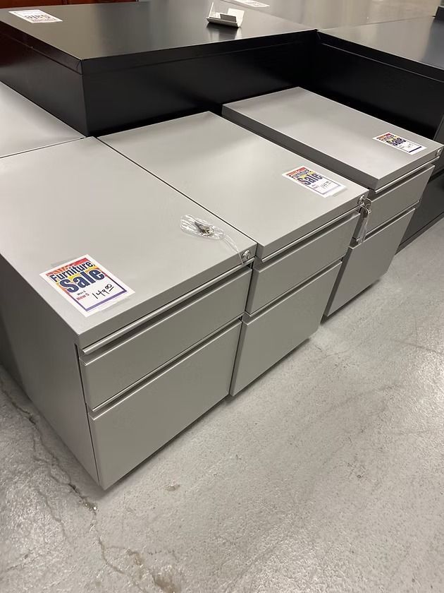 Three gray metal filing cabinets on a concrete floor, with a black cabinet behind them.