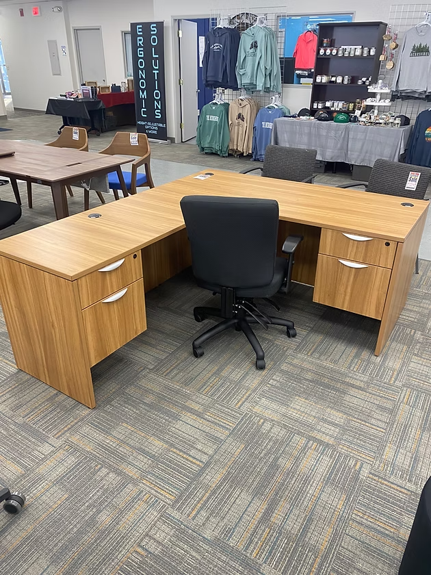 L-shaped wooden office desk with black chair in a store.