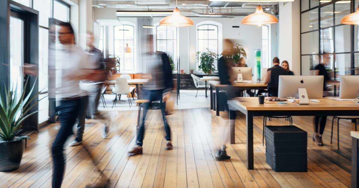Blurred office scene with people walking and working at desks.