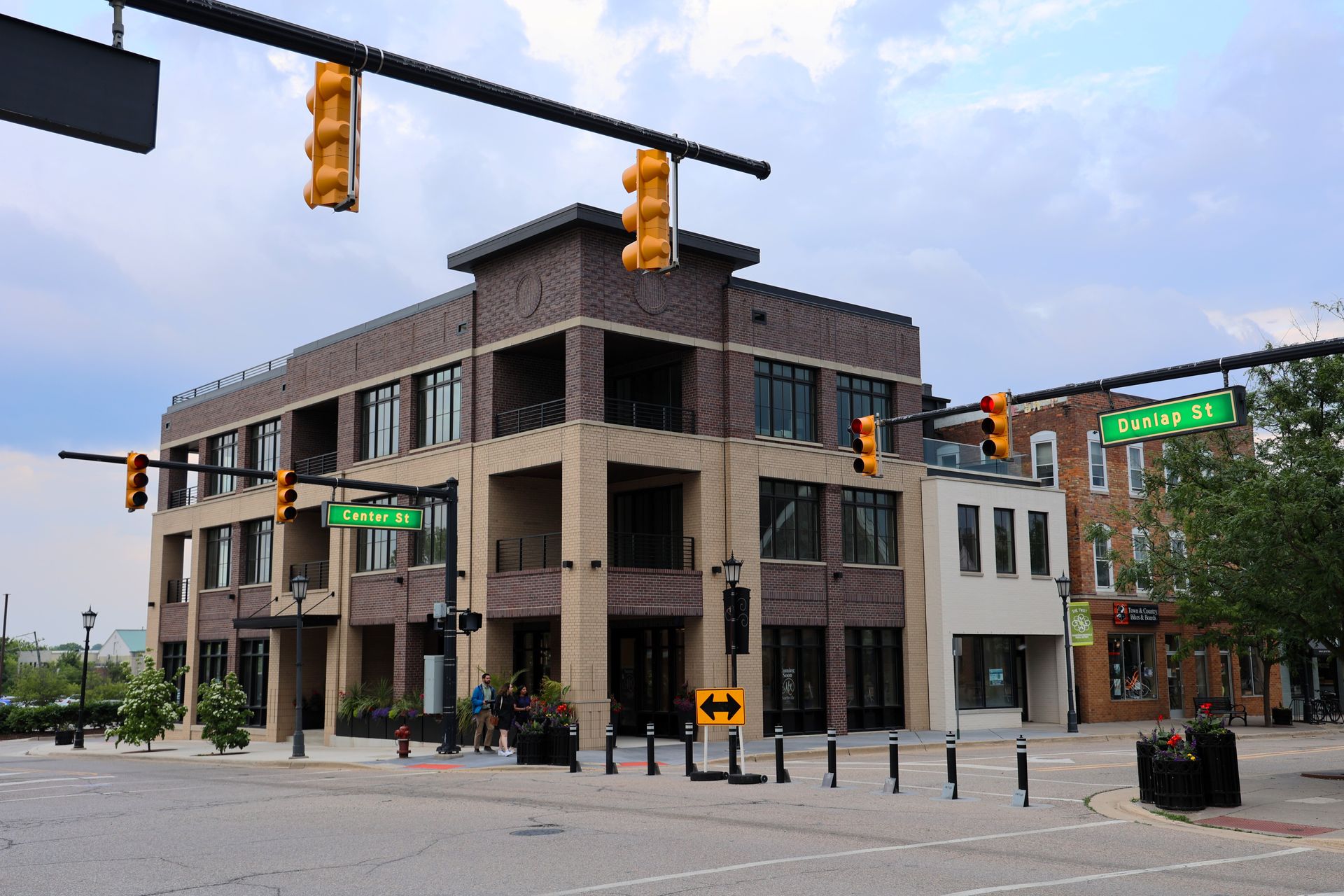 Multi-story brick building at a street corner with traffic lights, signs, and a cloudy sky.