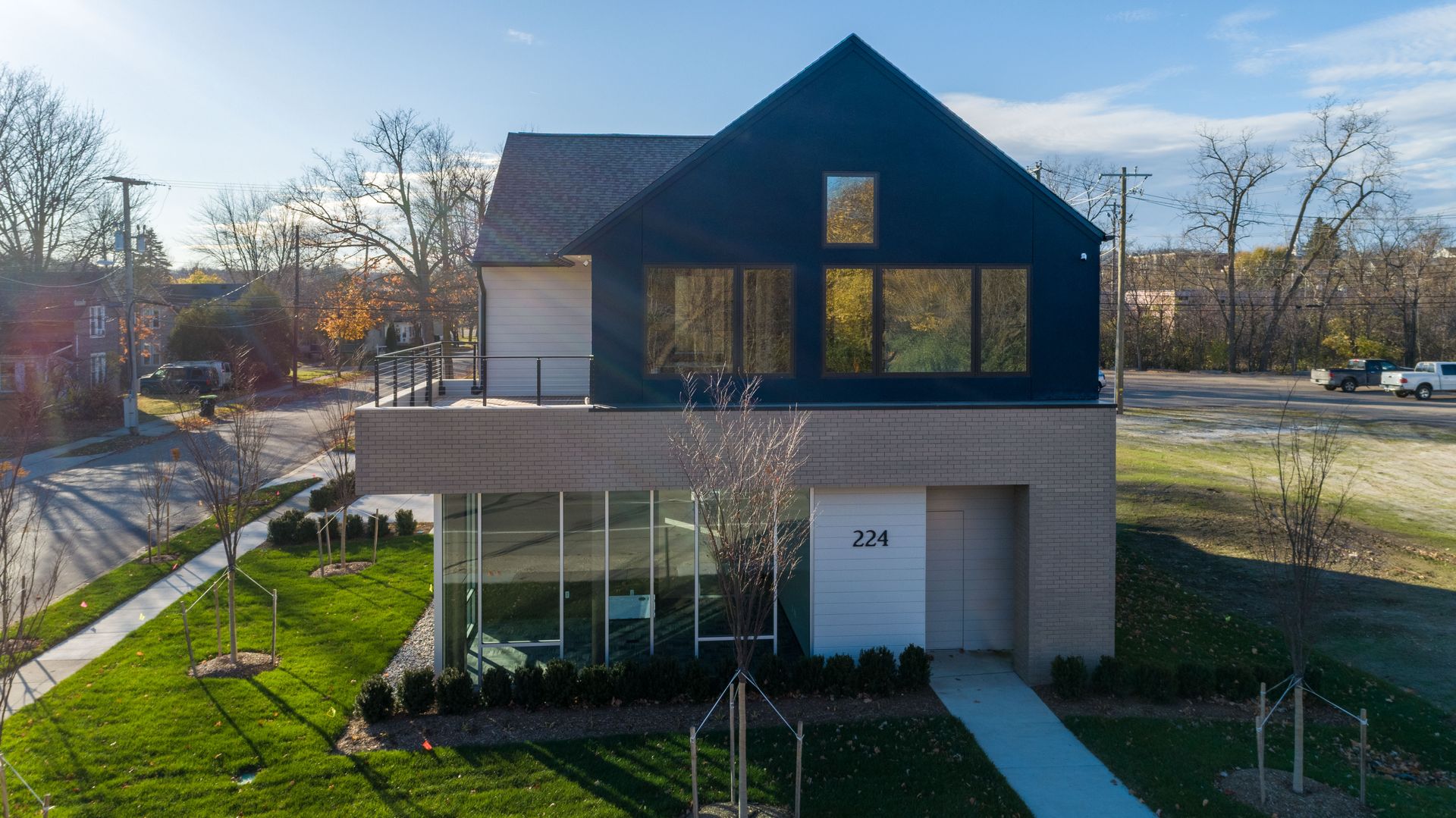 Modern two-story house with black upper level, glass front, brick accents, and a blue sky.