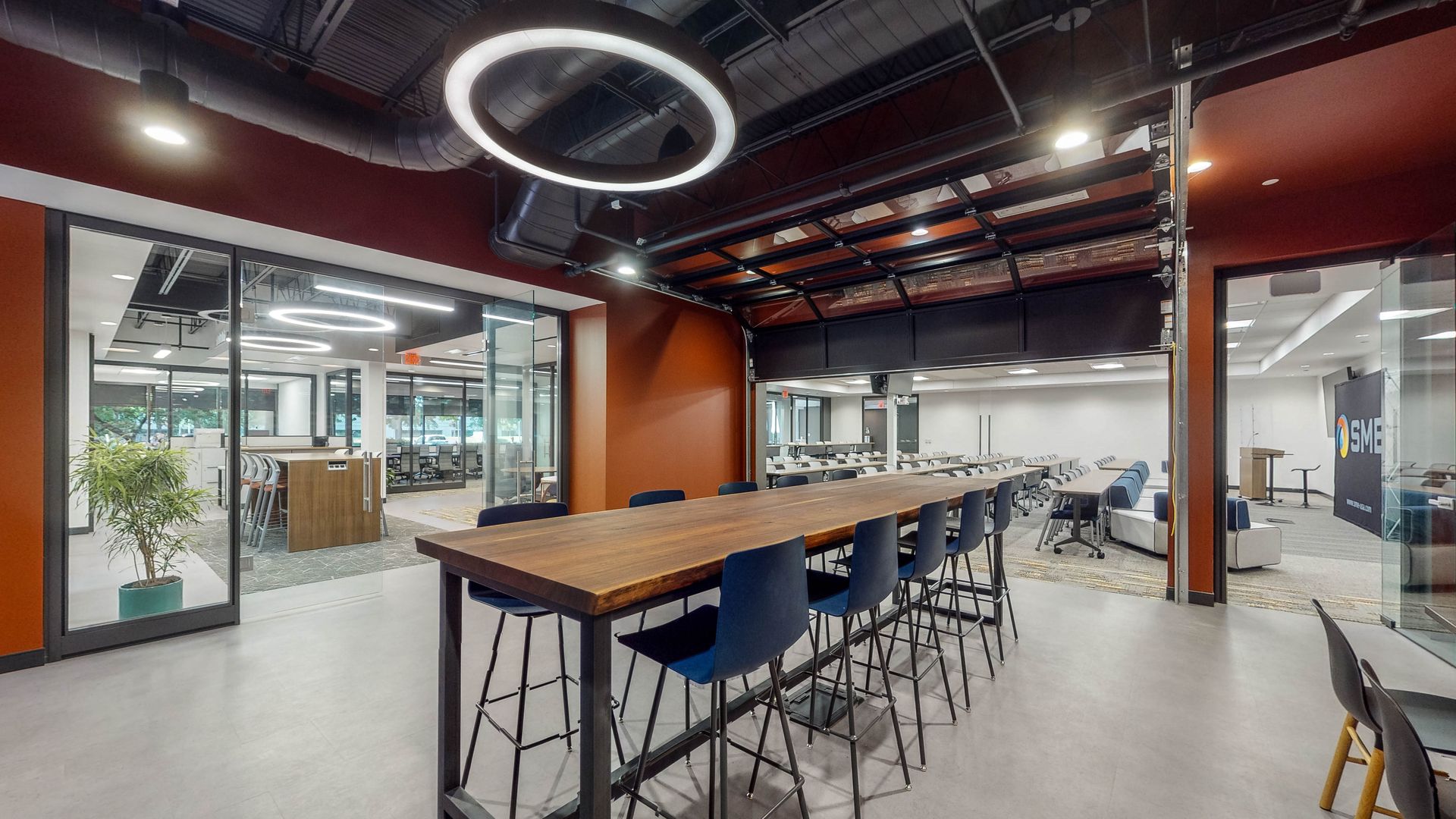 Modern office space with long table, blue chairs, glass walls, and a circular light fixture.