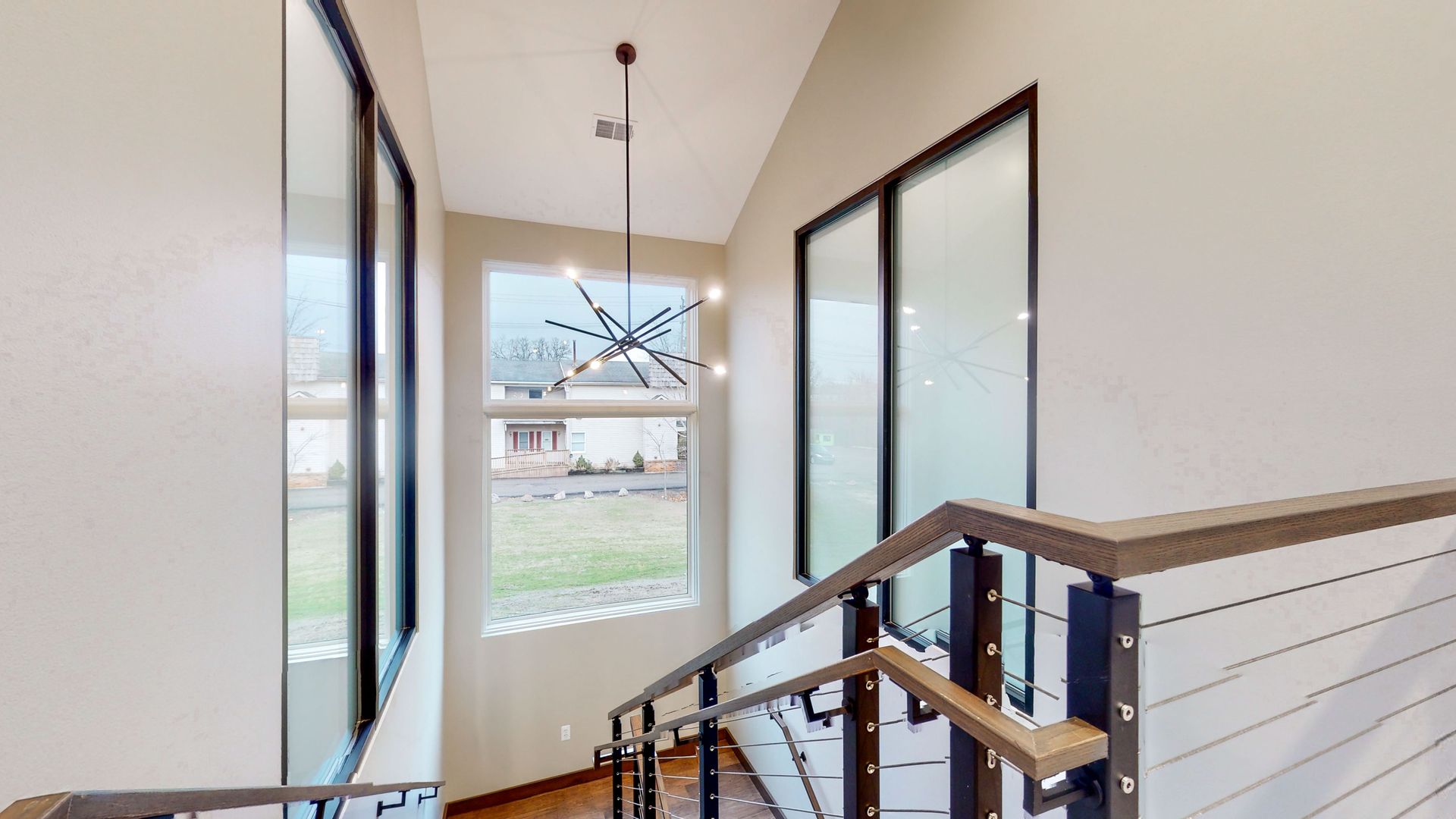 Staircase with large windows, a modern chandelier, and a view of a lawn and houses.