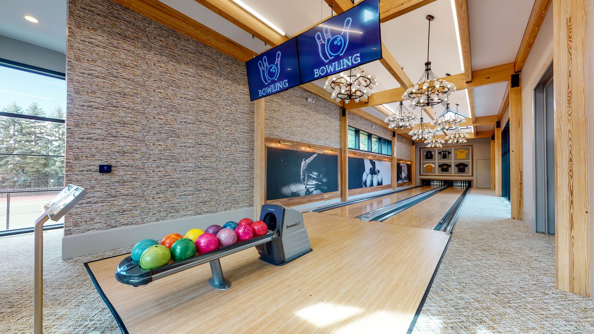 Bowling alley with wood accents, colorful balls, and screens displaying logos and art.