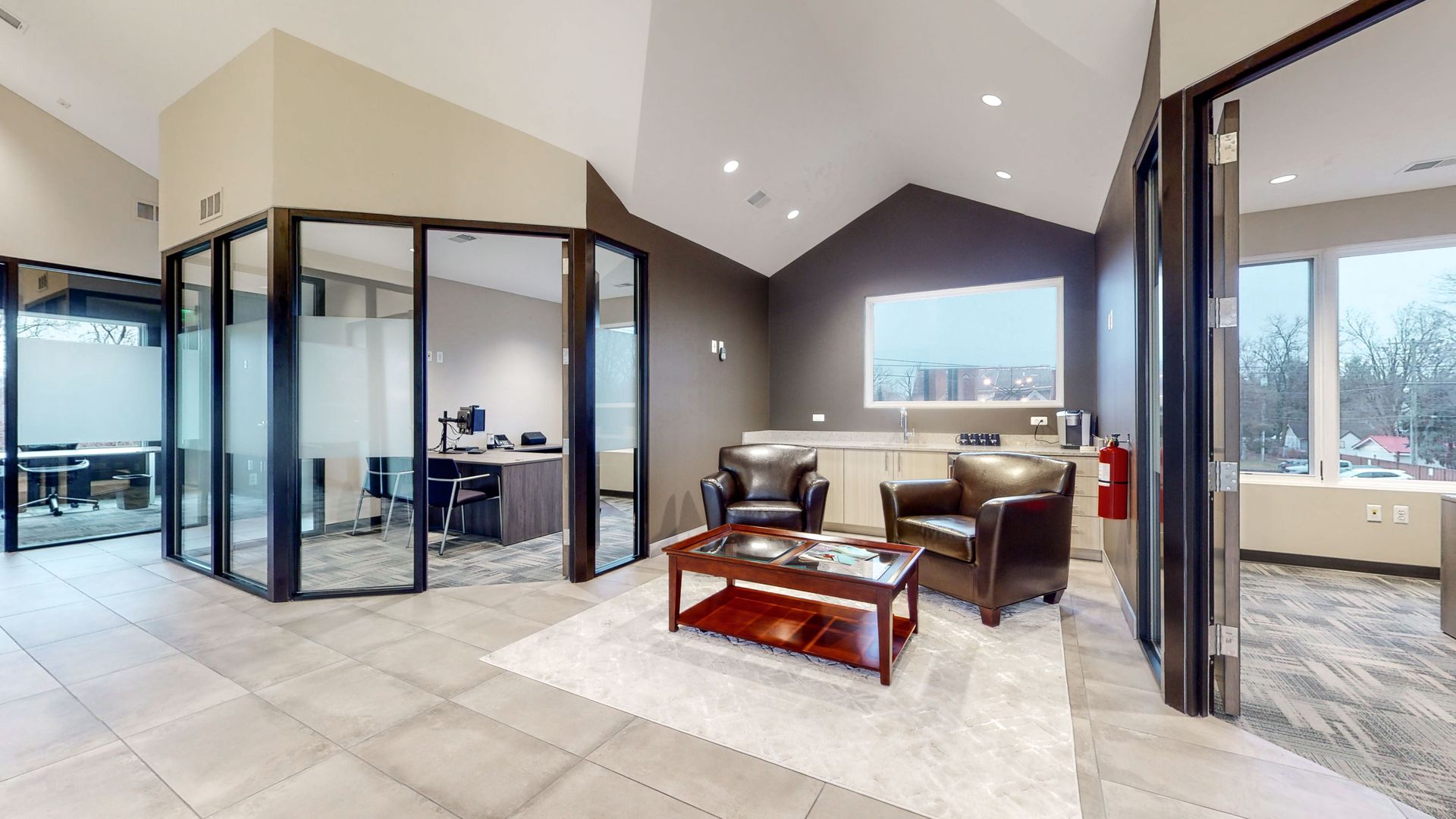 Modern office interior with leather chairs, coffee table, and glass-walled offices.
