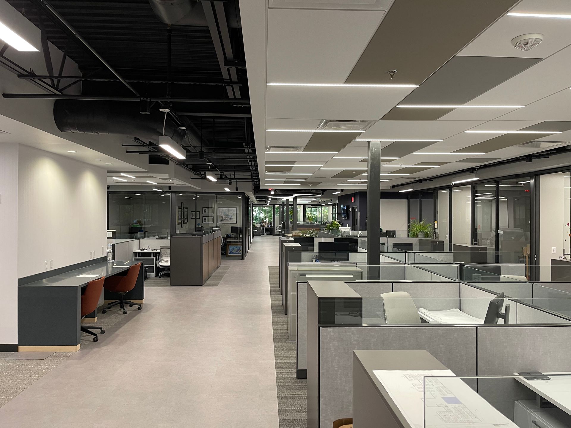 Modern office space with cubicles, desks, and glass-walled offices. Neutral colors, open layout.