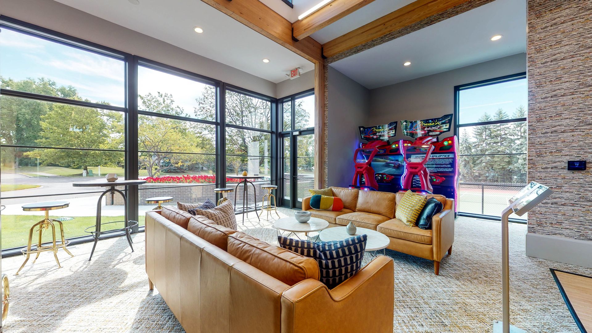 Modern lounge with leather sofas, arcade games, and large windows overlooking a green space.