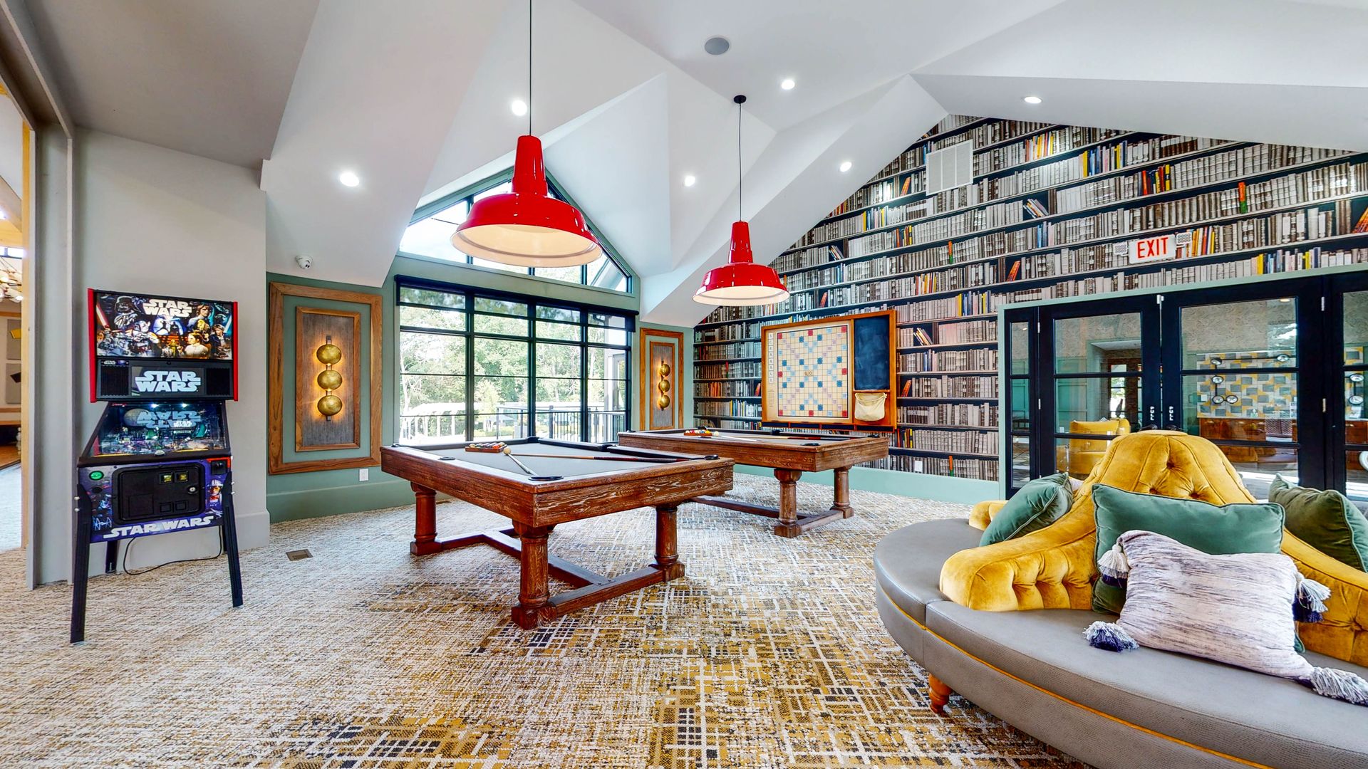 Game room with pinball, pool tables, library wall, and red pendant lights.