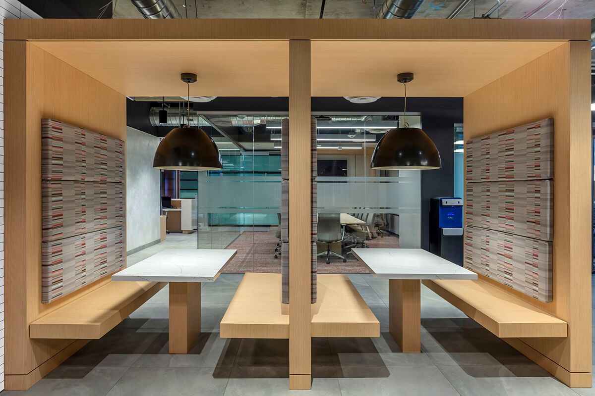 Modern wooden booth seating with white tables and hanging pendant lights in a quiet restaurant corner