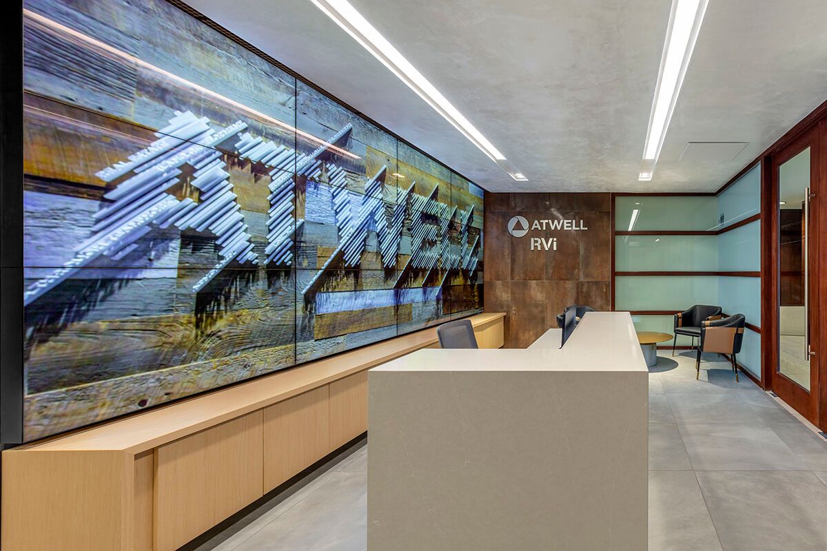 Modern office lobby with a long digital display wall, wood bench, and reception desk in a bright hallway