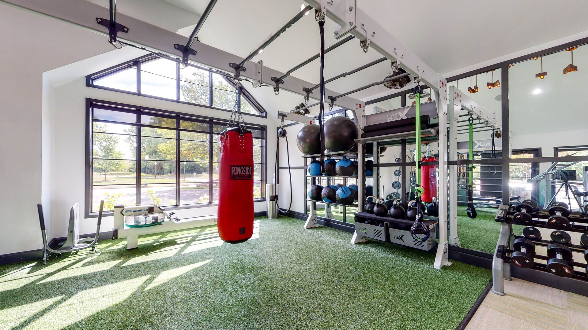 Gym interior with training equipment, featuring a red punching bag, weights, and large windows.