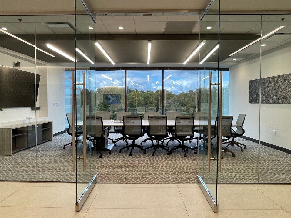 Glass-walled conference room with a long table, black office chairs, and a city view outside