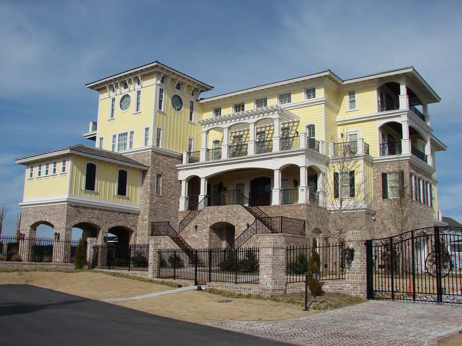 Yellow mansion with stone accents, balconies, and a wrought iron fence under a blue sky.