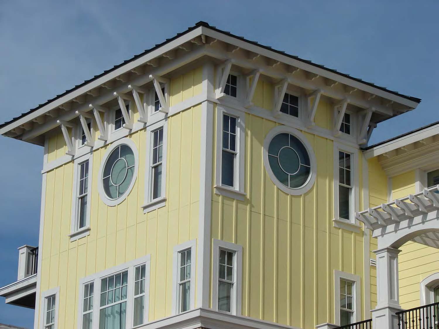 Yellow building with white trim and decorative supports, round and rectangular windows.