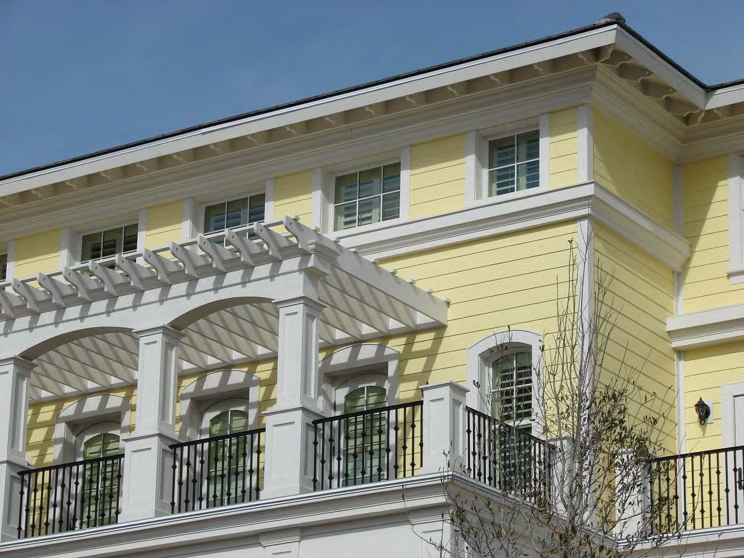 Yellow building with a white pergola, black railings, and small windows. Blue sky in the background.