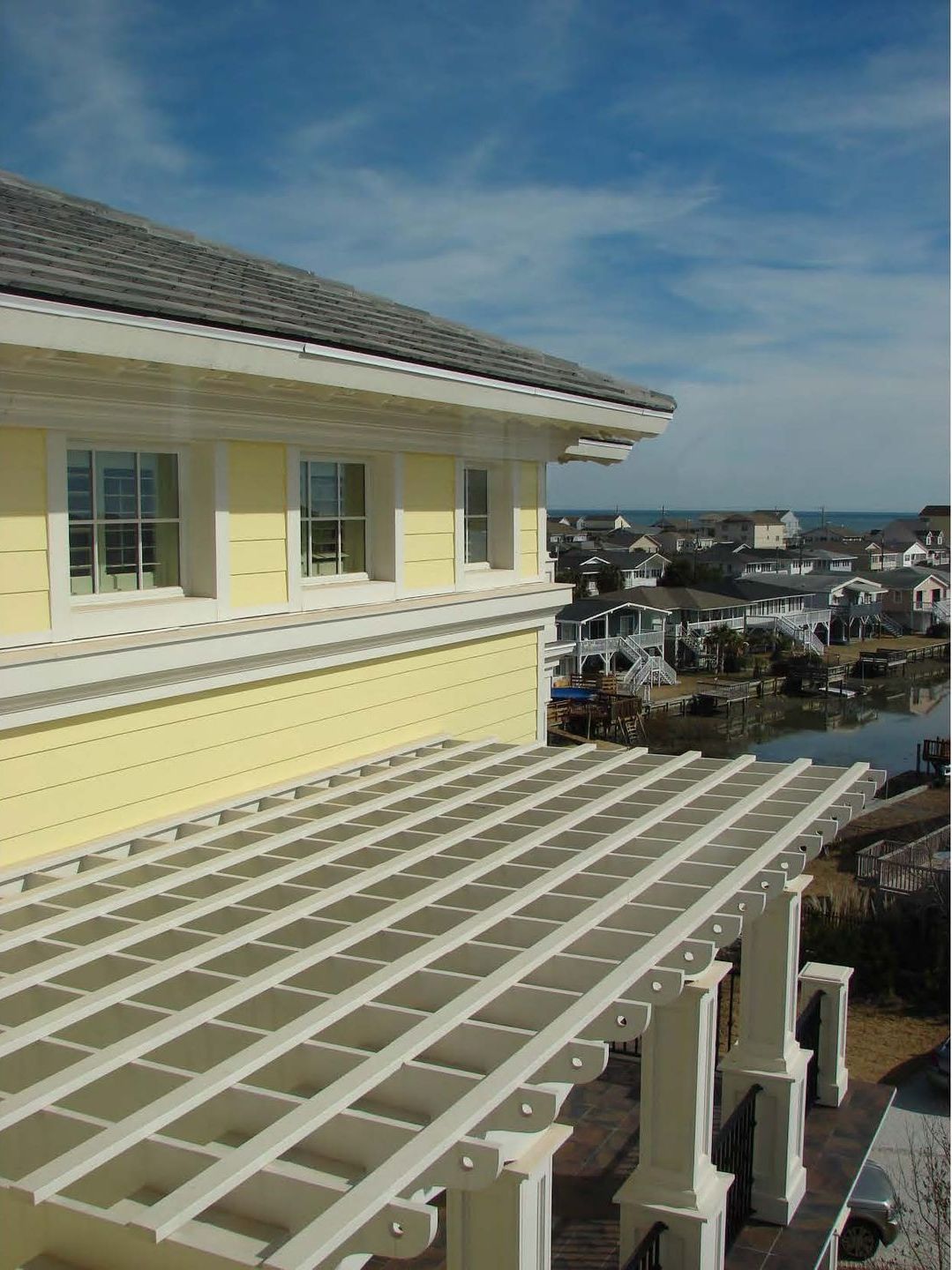 Yellow house exterior with pergola overlooking a coastal town under a blue sky.