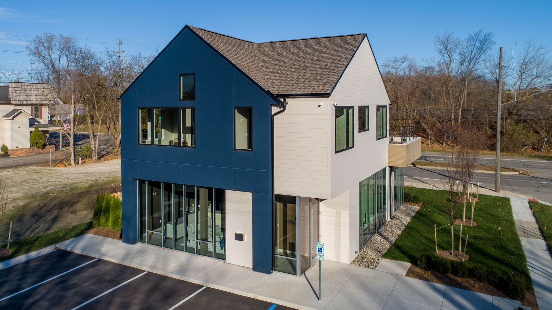Modern two-story building with blue and white exterior, large windows, and accessible parking space in front.
