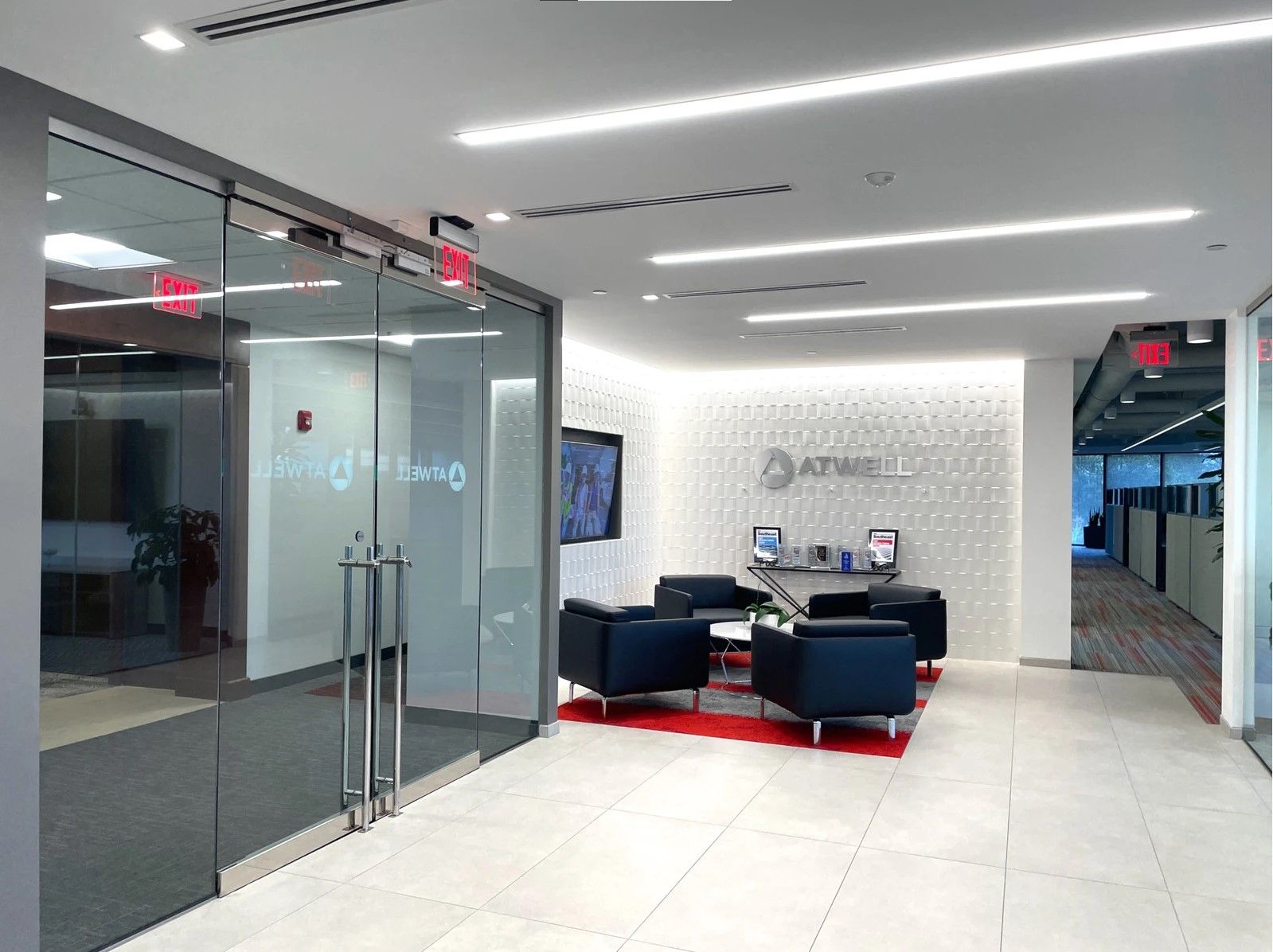 Modern office lobby with glass walls, blue seating, and a reception area with red carpet accents