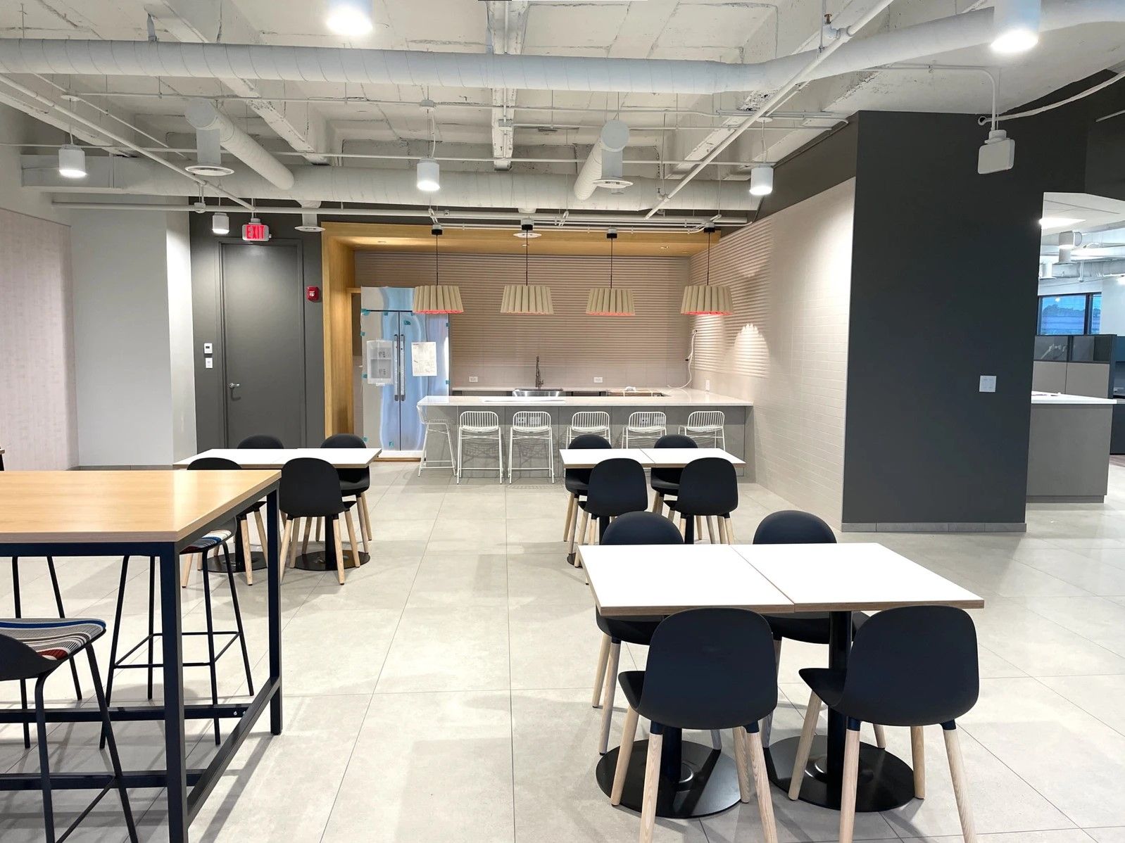 Modern cafeteria seating area with black chairs, wood tables, and a service counter in the background