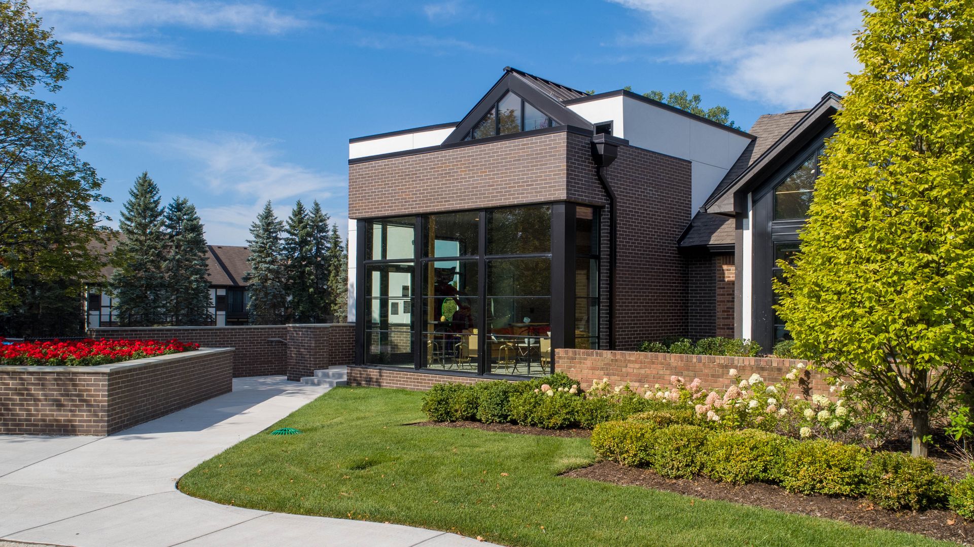 Modern building with glass entrance, brick, and landscaping on a sunny day.