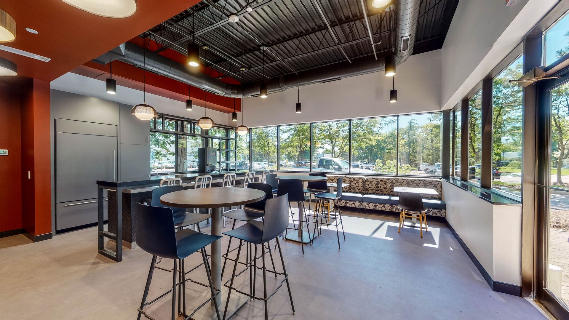 Interior of a modern dining area with tables, chairs, and large windows overlooking a sunny outdoor view.