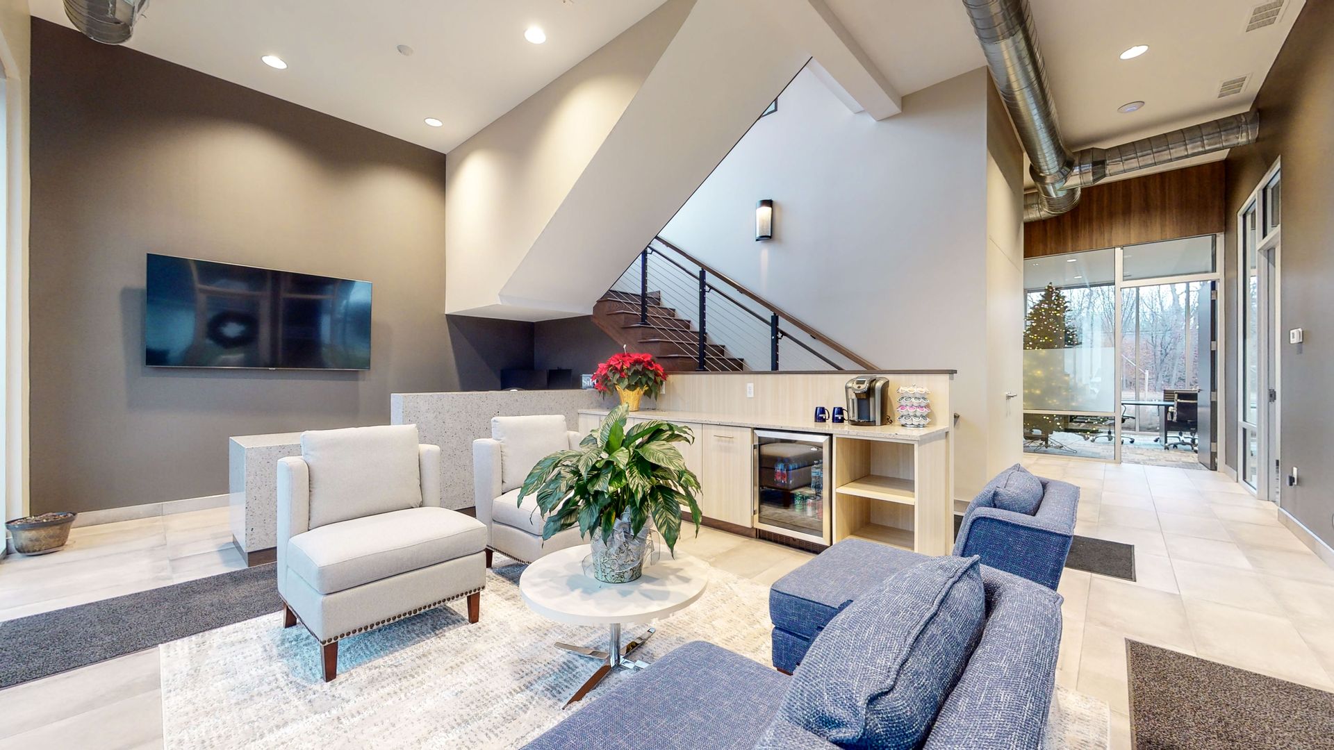 Lounge with seating, stairs, coffee station, and a TV. Modern design with gray, white, and blue accents.