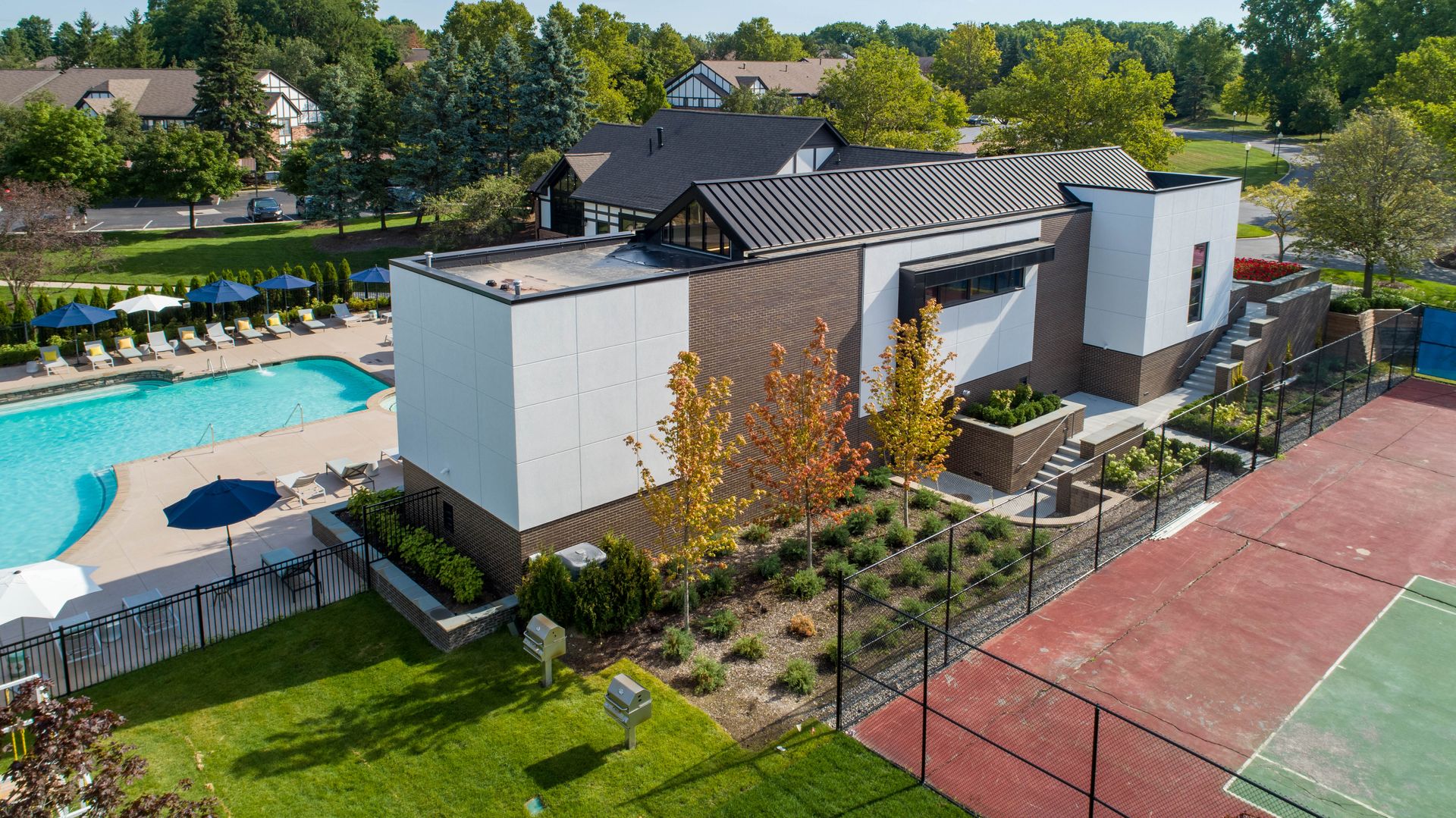 Modern community center with pool, tennis court, and landscaping on a sunny day.