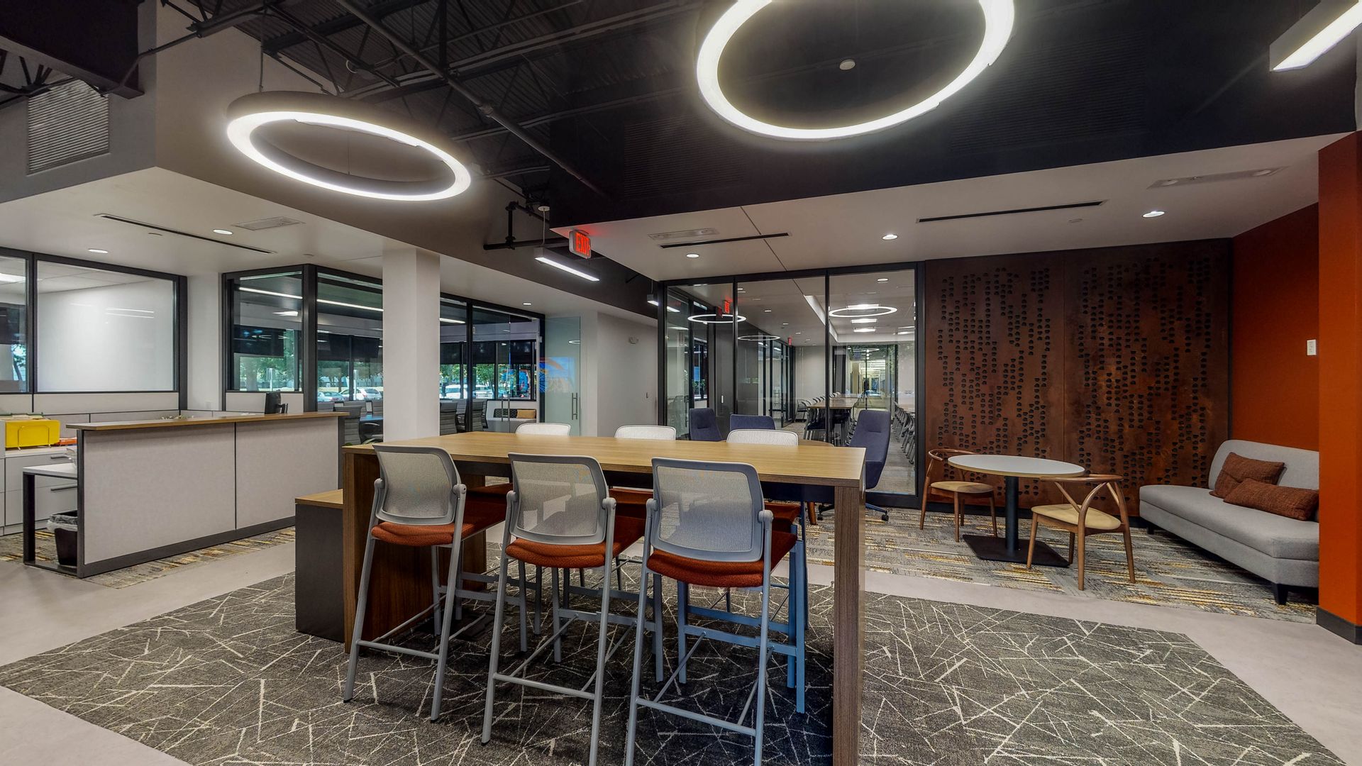 Modern office interior with collaborative space, long table with stools, lounge seating, and large windows.