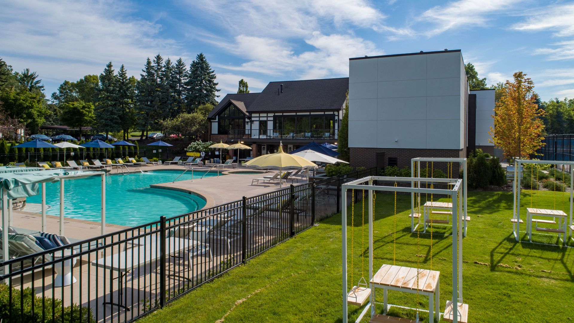 Pool and building, outdoor scene with blue water, green grass, trees, sunny day.