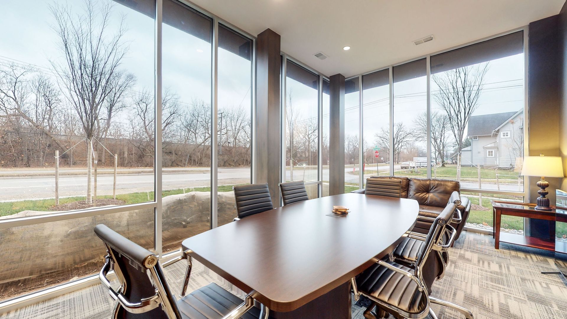 Conference room with large windows overlooking a street and trees; a long table with chairs.