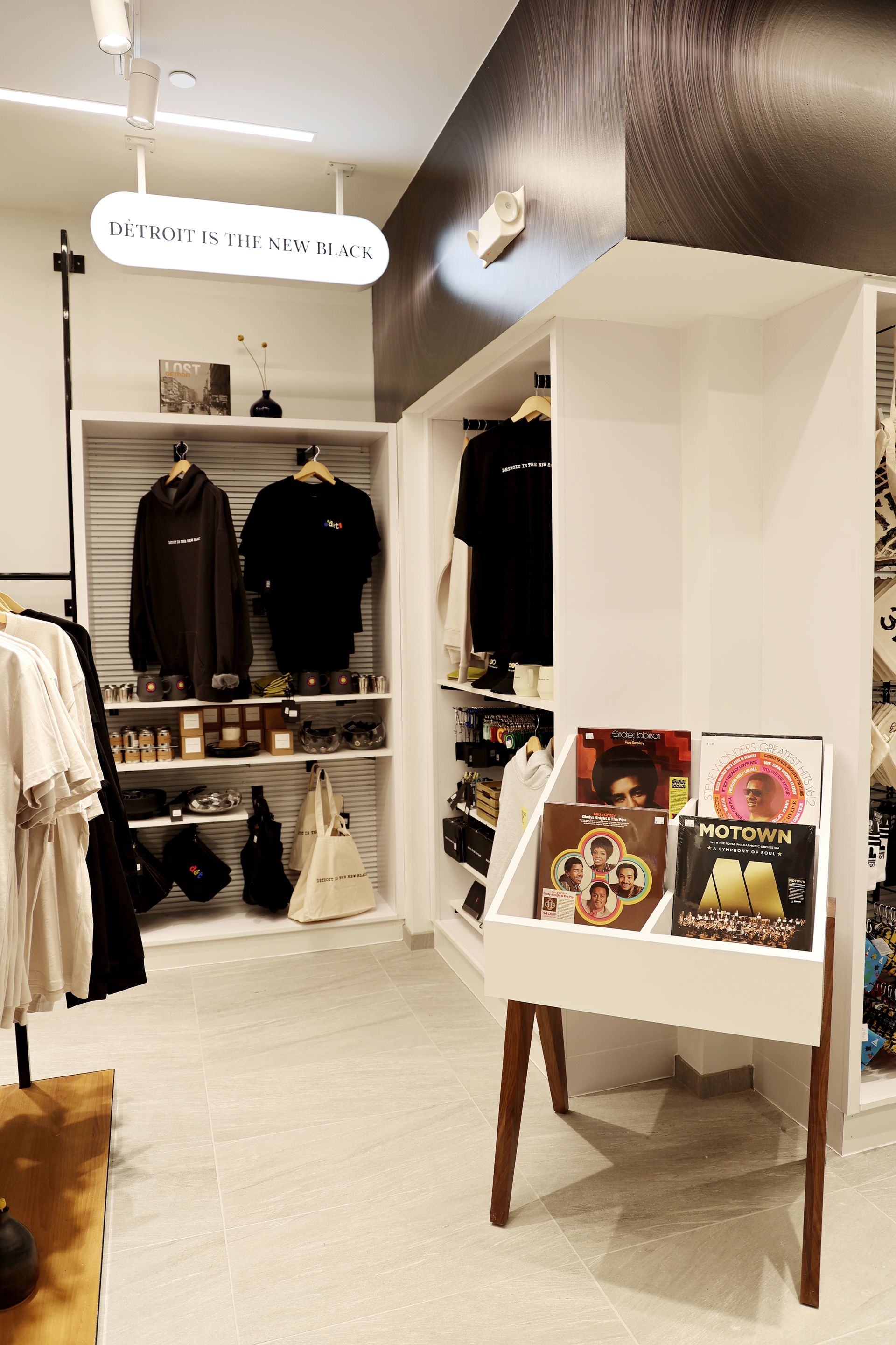 Inside a clothing shop, racks of apparel and records. White shelves, wood accents.