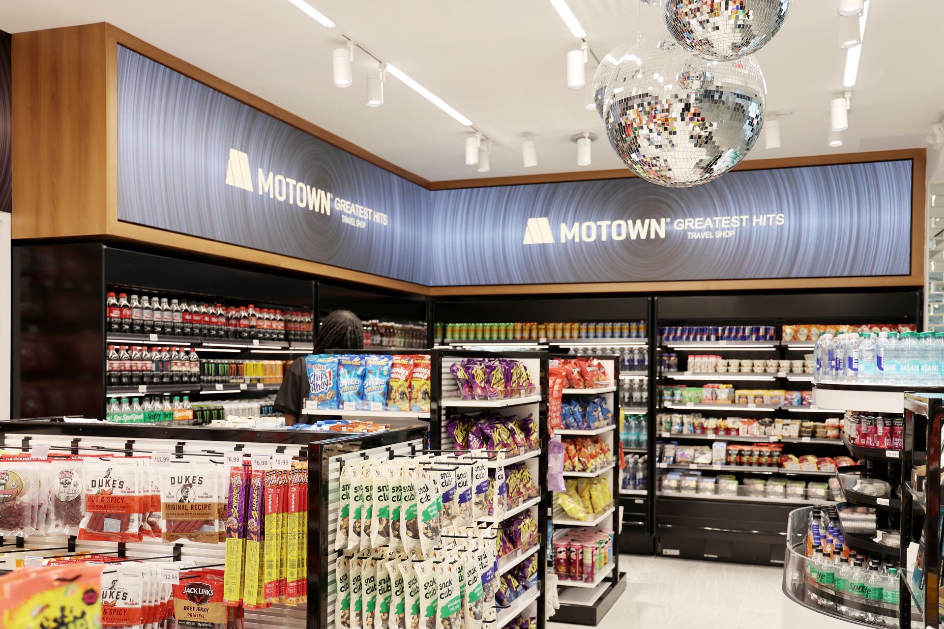 Interior view of a modern store aisle with shelves of products, disco balls hanging from the ceiling.
