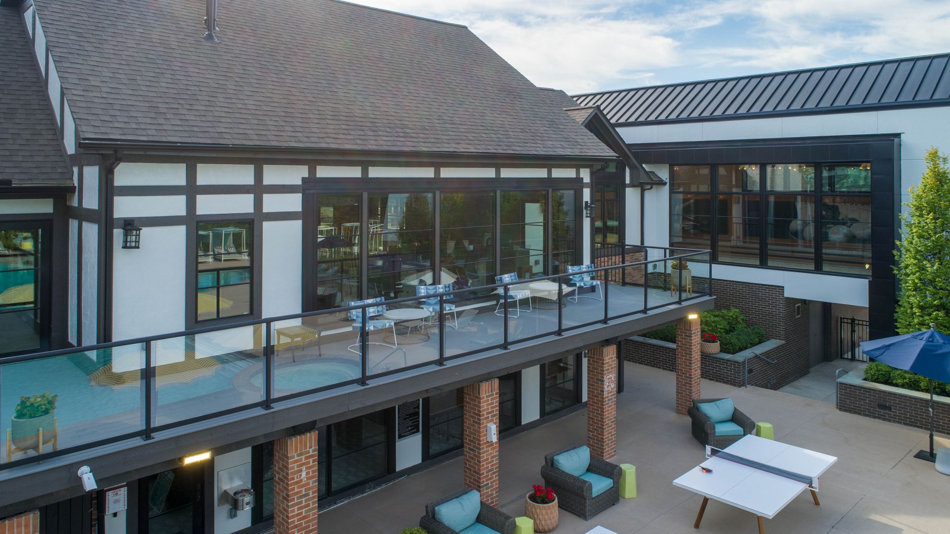 Two-story building with deck and patio. Black, white, and brick facade. Blue chairs and ping pong table.