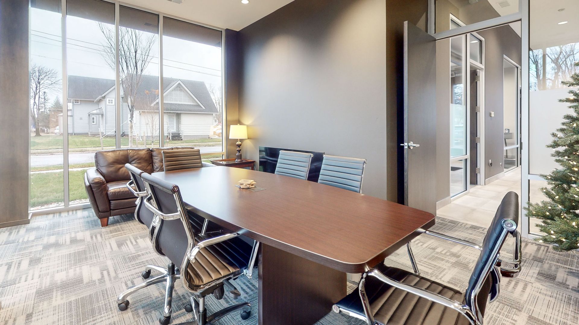 Meeting room with large table, chairs, sofa, and windows looking outside.