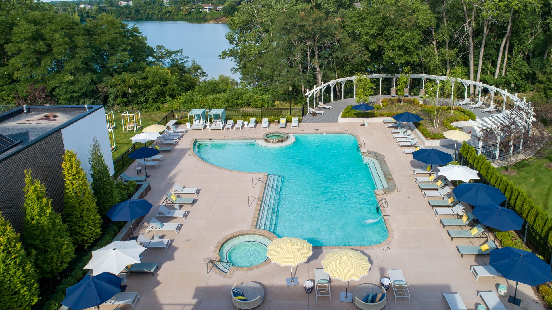 Pool with turquoise water, lounge chairs, and umbrellas, near a lake and trees.