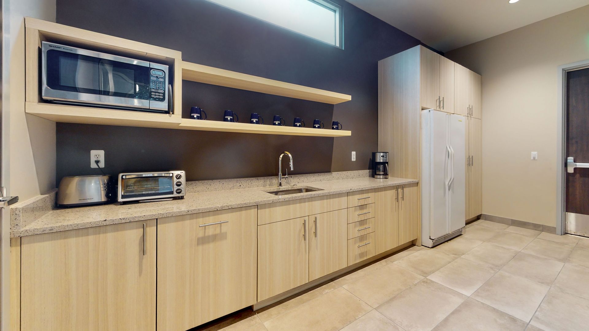 Kitchenette with microwave, cabinets, sink, and refrigerator; neutral tones.