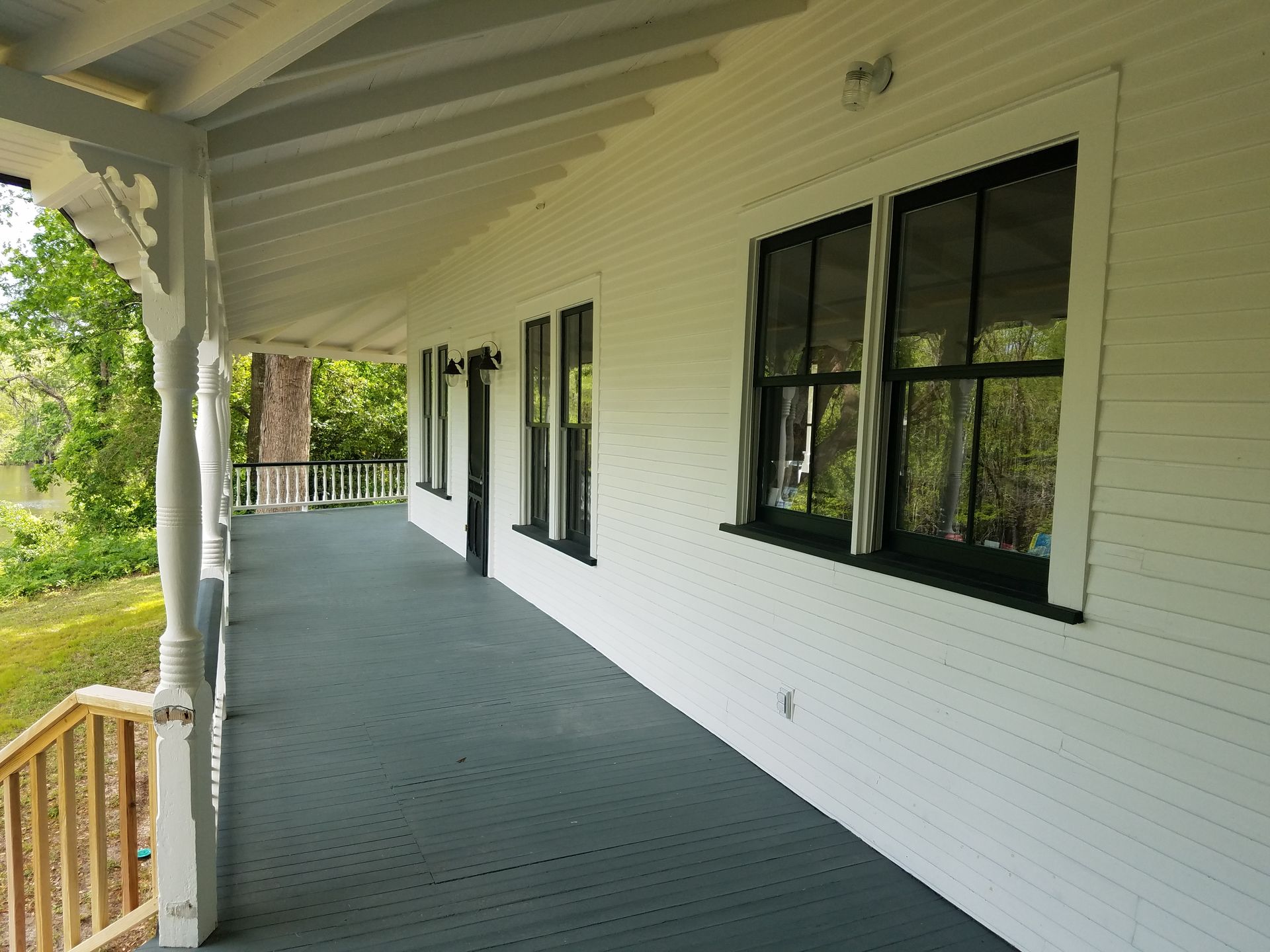 A white-painted porch with dark trim and windows, overlooking a green lawn and trees.
