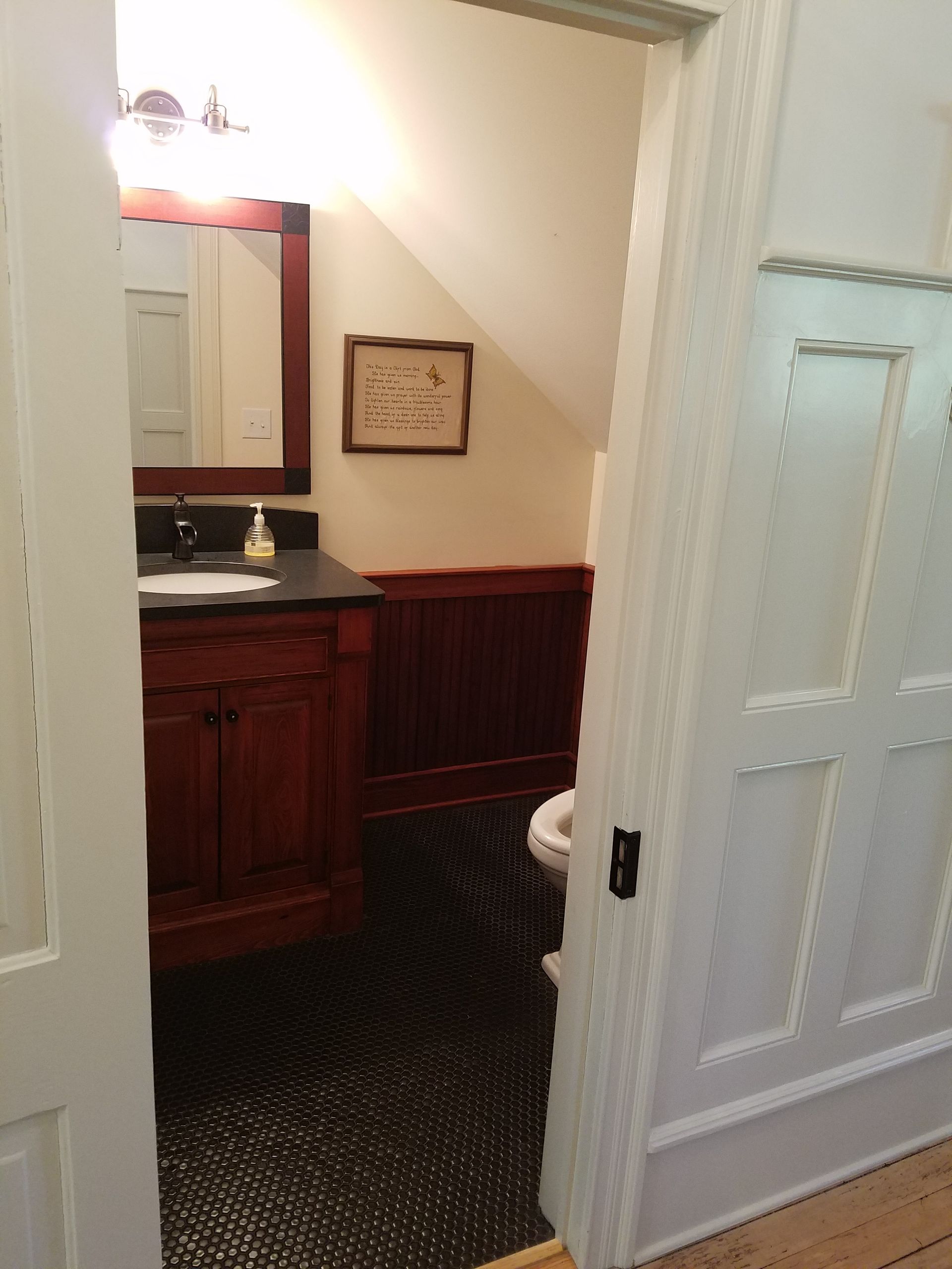 View into a small bathroom with dark floors, a vanity, toilet, and wood paneling.